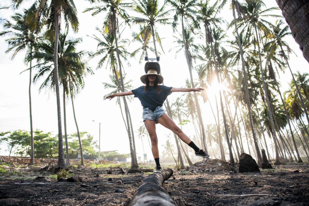 A young woman balances on a log amidst a tropical palm grove, exuding a carefree and adventurous vibe.