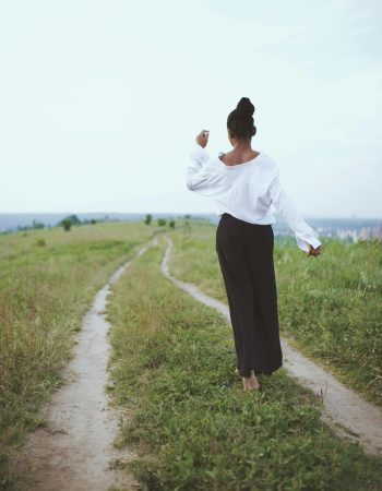 A woman walks barefoot on a grassy rural path, embracing nature and solitude.